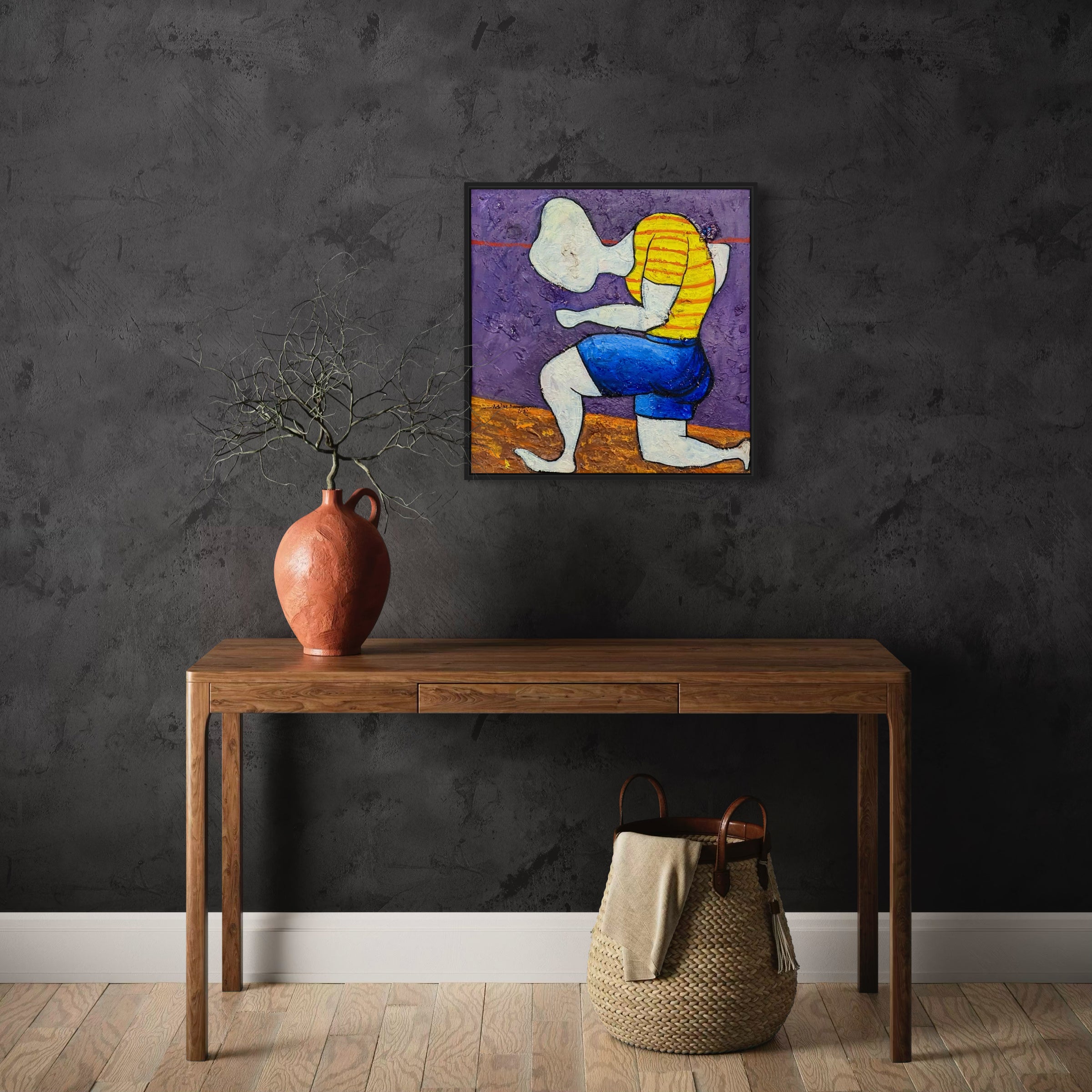A minimalist wooden table with a terracotta vase and bare branches sits against a dark wall. Above, "Dance Of Nature" by Achike Anayo, an expressionist painting in a black tray frame, is displayed. A woven basket rests below the table.