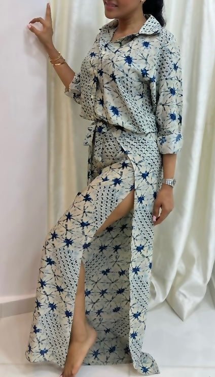 A woman models bibianna.co.uk’s Adire Batik Chiffon Multiway 2 Piece Top & Wrap Pant Set—blue and white geometric print, high slit pant—barefoot against a white curtain, accessorized with bracelets and a watch. Her face is partially out of frame.