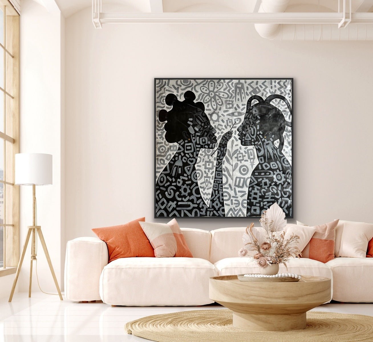 A modern living room with a white sofa, peach and orange pillows, a round wooden coffee table with dried flowers, and Afuope Opeyemi’s Monochrome Large Acrylic Painting on Canvas "Adornment" above the couch. Light pours in from tall windows.