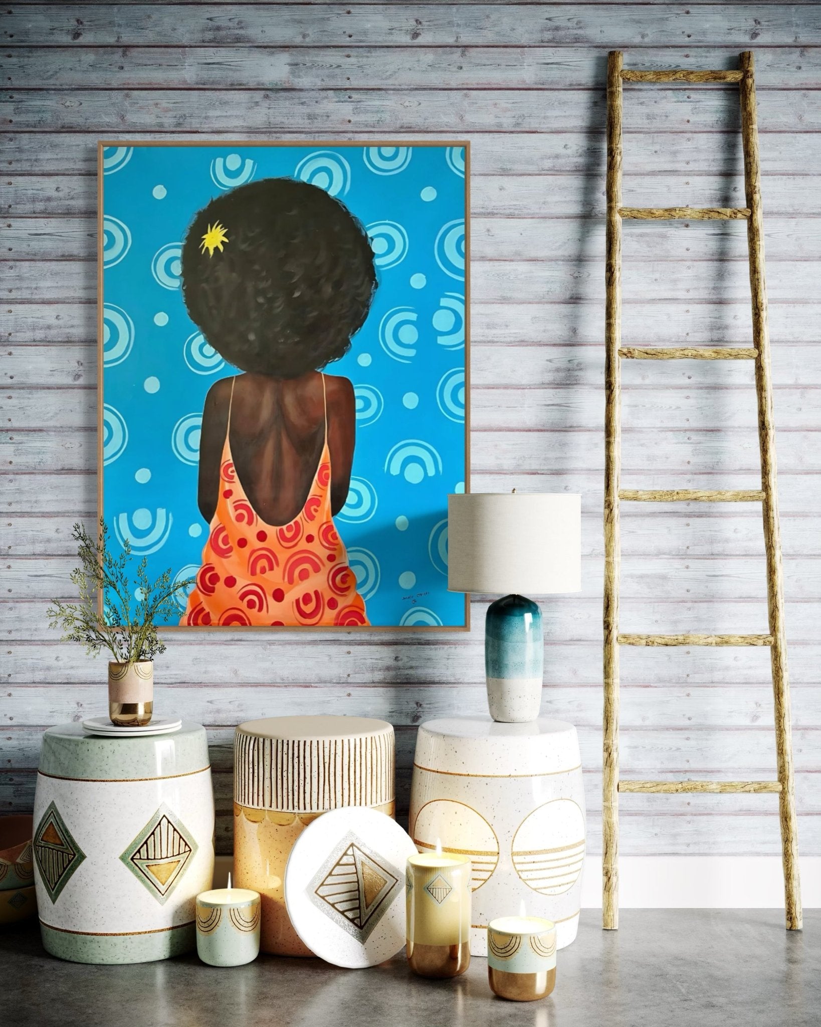 A cozy room with a wooden ladder, three decorative stools, candles, and a lamp. The wall features “My Afro,” a vibrant contemporary African portrait by Afuope Opeyemi, depicting a woman with dark curls in an orange dress.