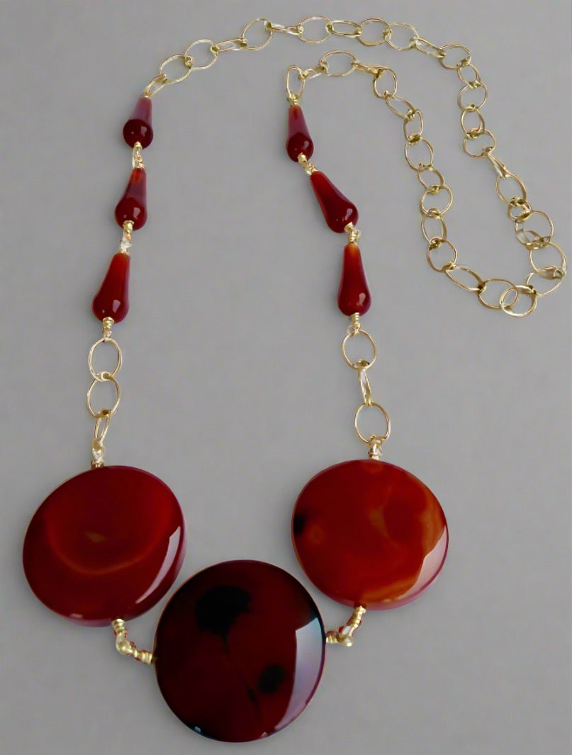 The Ariaba Agate and Carnelian Drop Necklace by bibianna.co.uk features three large red stones at the center, accented with carnelian beads and gold links for an exquisite statement piece.