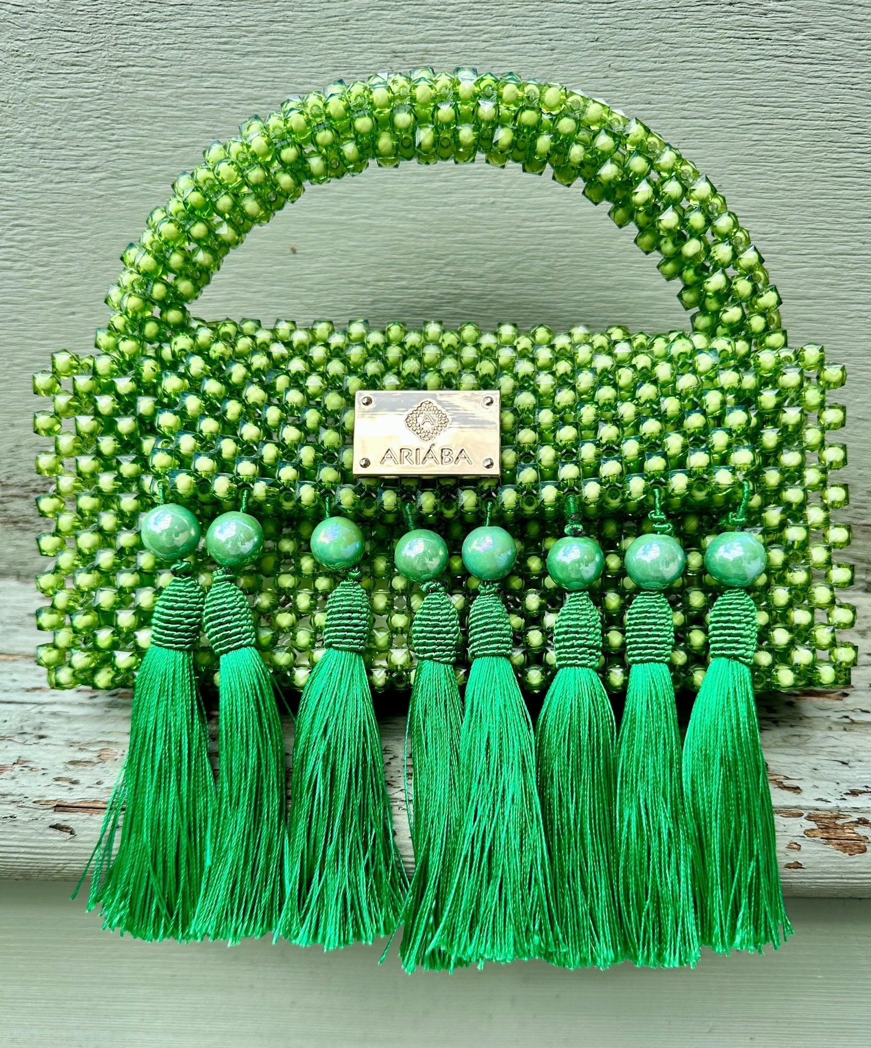 The Ariaba Ira Tassal Bag, Green by bibianna.co.uk is a small handcrafted accessory featuring green beads with tassels and a gold nameplate—a standout Nigerian piece perfect for elevating your look.