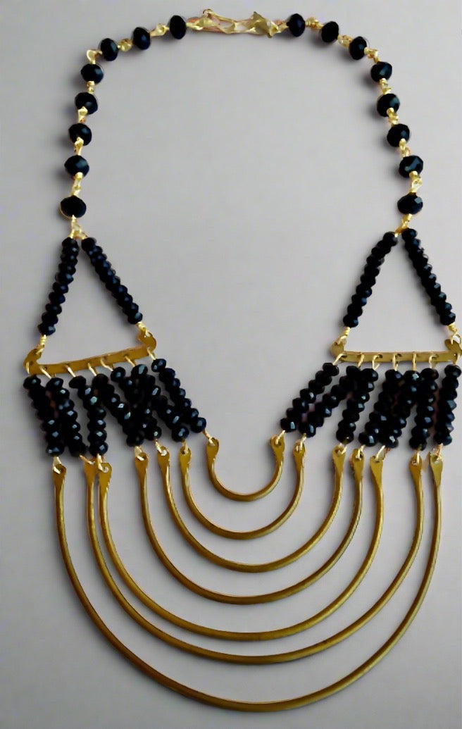 The Ariaba Onyx and Bronze necklace from bibianna.co.uk features five bold bronze curved bands and layered strands of small black beads, connected with gold links for a striking, geometric, handmade-inspired design.