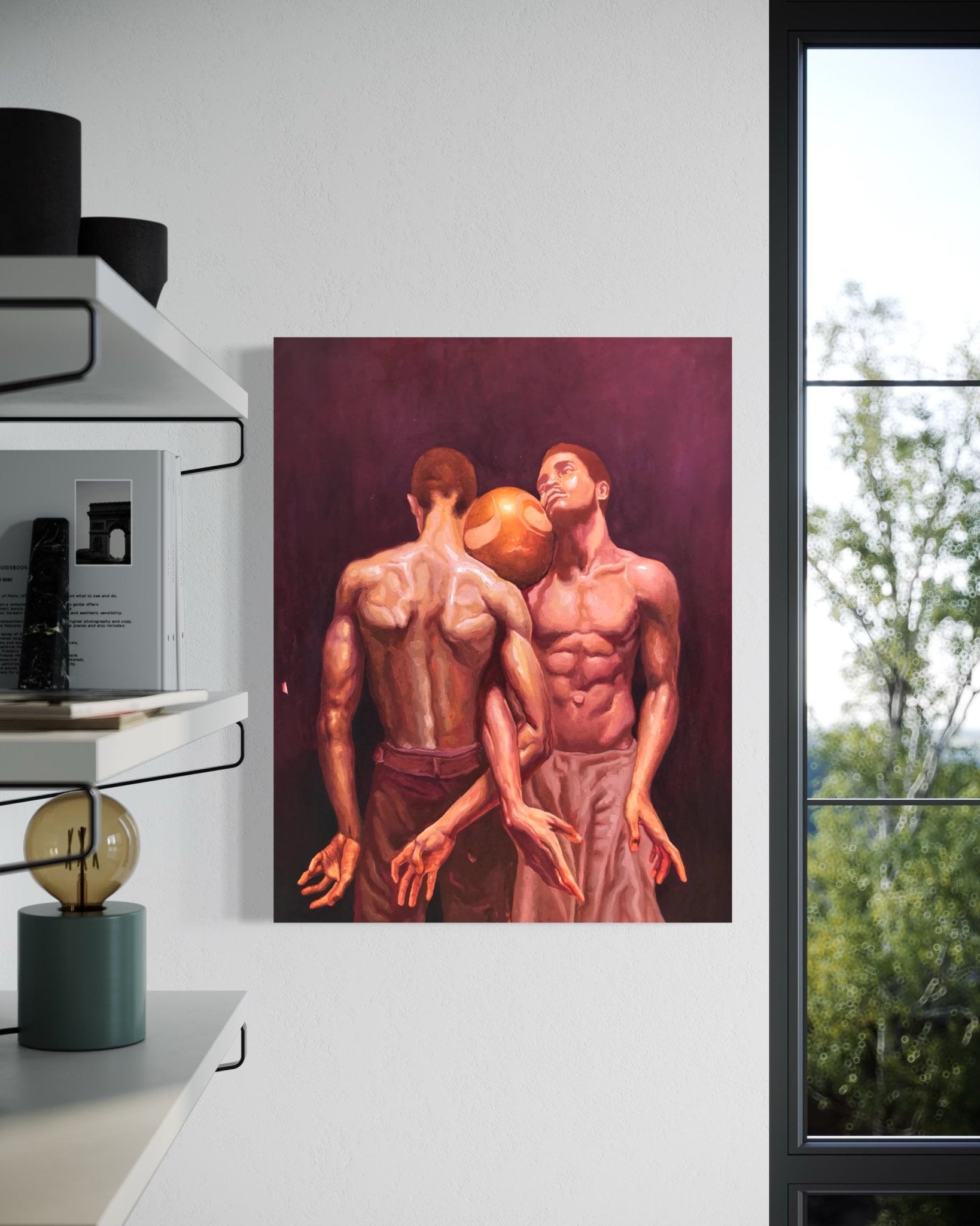 Attached" by Emmanuel Ugwu, a soft realism oil painting of two shirtless men with muscular backs and a golden ball between their heads, hangs on a white wall near a window with trees outside, shelves, and a lamp creating an intimate setting.