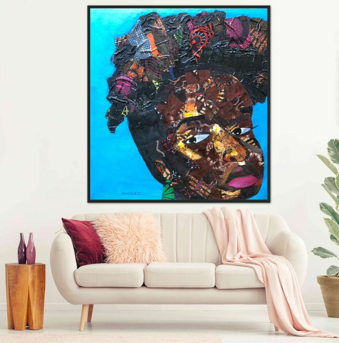 A living room with a white couch, pink pillow, and pink blanket. Above the couch hangs "Ankara Lady" by J.O. Aransiola, a vibrant acrylic on canvas of a woman with textured hair against blue. A potted plant is to the right.