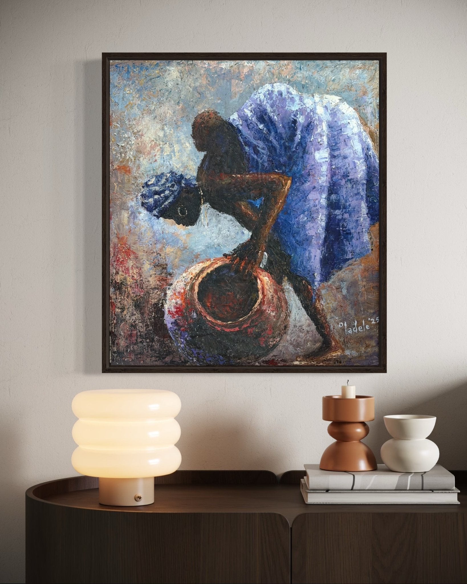 Backed Up" by Sunday Oladele is an original framed painting depicting African motherhood—a woman in a blue dress bends with a large clay pot—perfect to hang above a modern wooden table with decor accents.