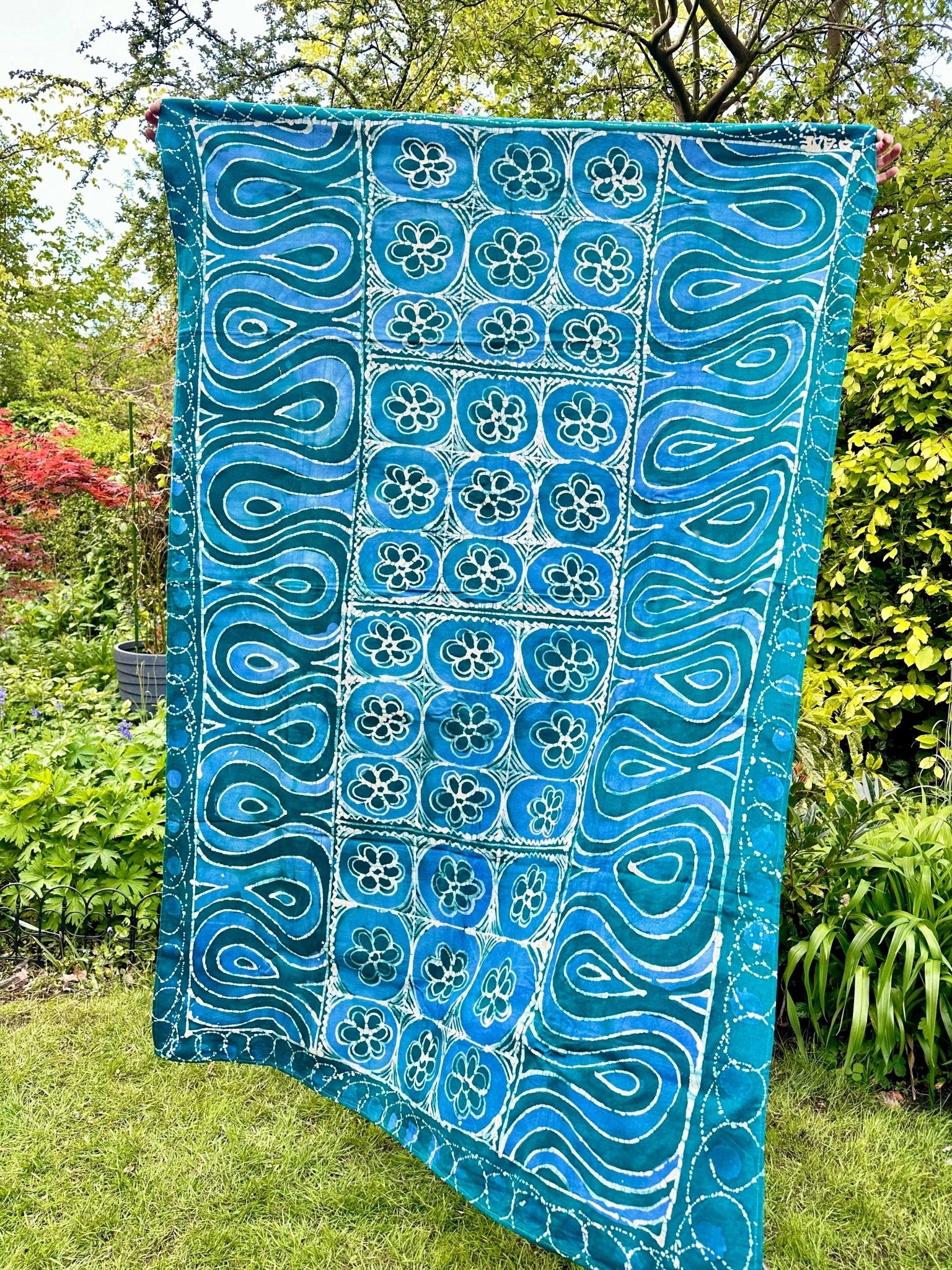 The Batik table cloth/beach or picnic blanket by bibianna.co.uk is handmade in Nigeria from 100% cotton, showcasing blue and teal batik with white floral and swirling patterns—perfect for your home, outdoors, or picnics.