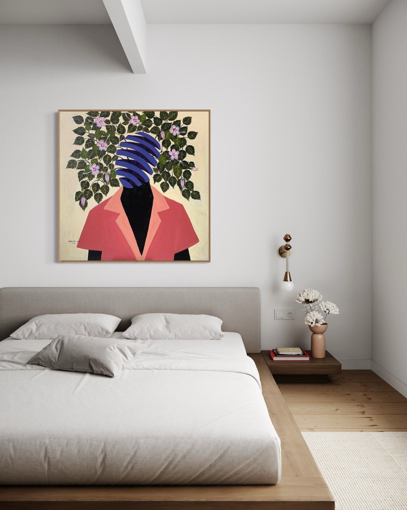 A modern bedroom features a low wooden bed, neutral bedding, a side table with flowers, and "Beyond Me" by Ayorinde Ayobami Lekan—a large framed mixed media canvas above the bed showing a faceless figure in a red jacket with leaves and flowers.
