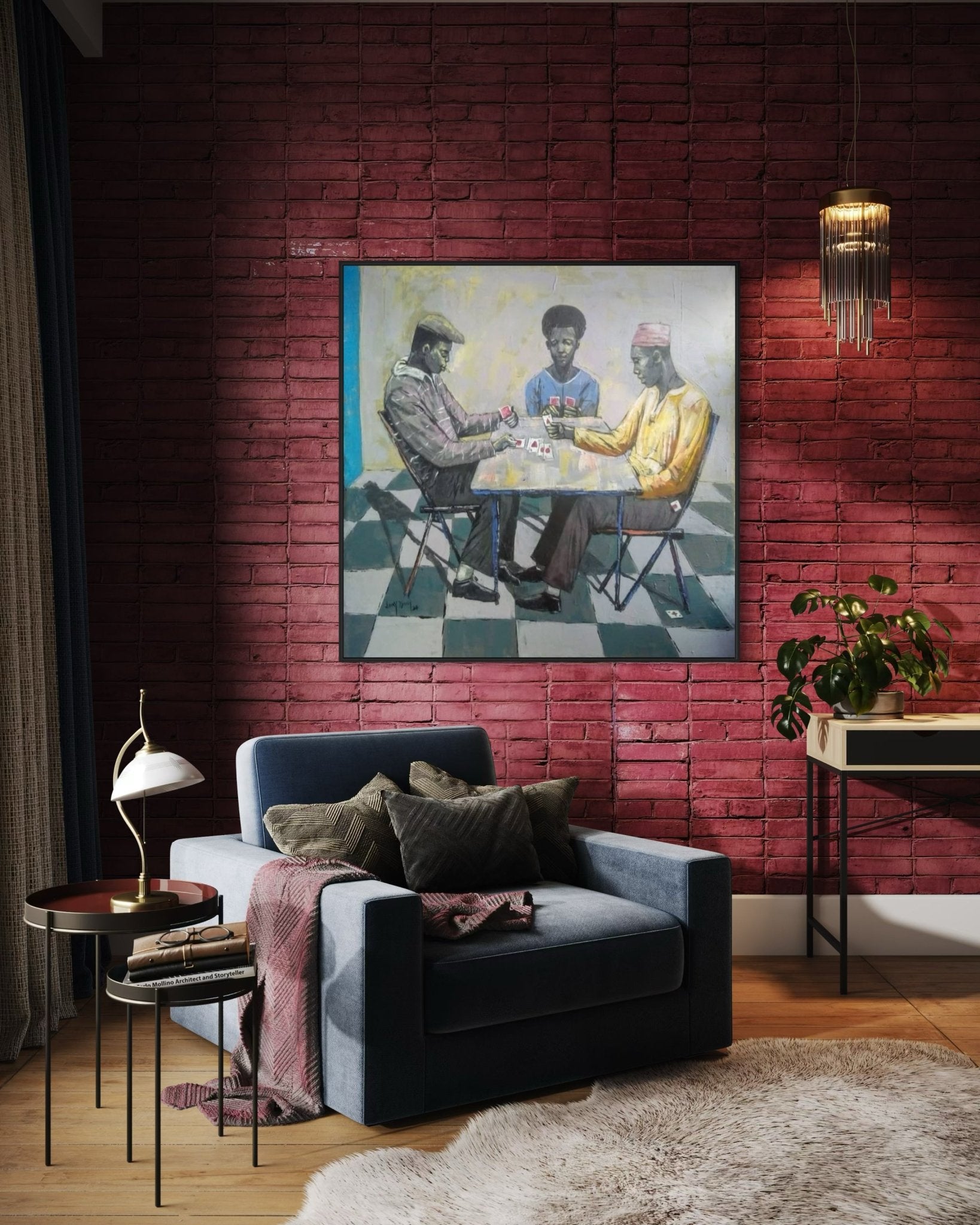 A cozy living room features a blue armchair, tables, lamp, and plant. The brick wall displays "Cartels" by Lucky Isaiah—an artwork of three people playing cards, sold with a certificate of authenticity. Warm lighting sets a relaxed mood.