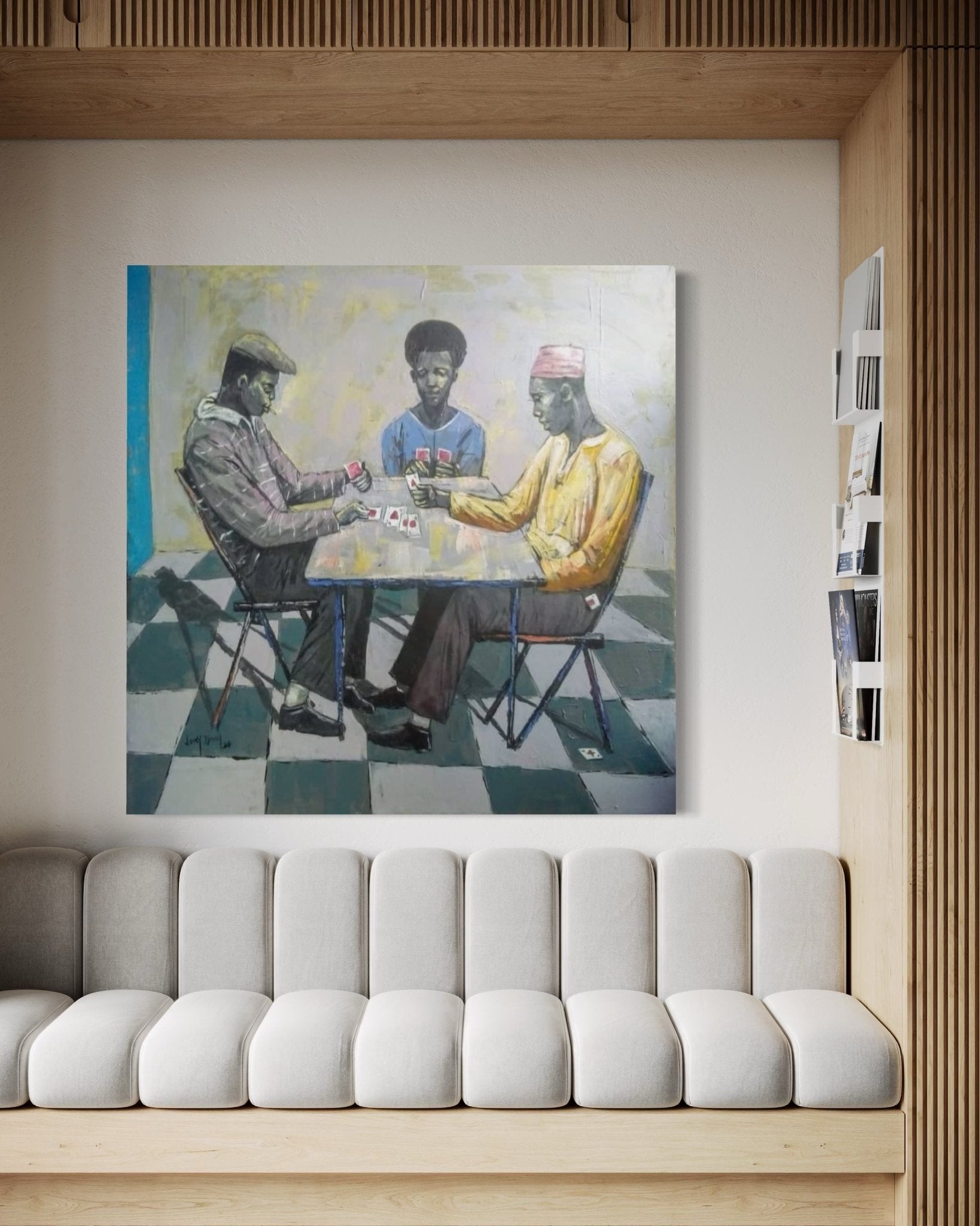 A modern living room with a light gray sofa and wood accents, featuring "Cartels" by Lucky Isaiah above the sofa—three men playing cards on a checkered floor. This hand-signed artwork includes a certificate of authenticity.