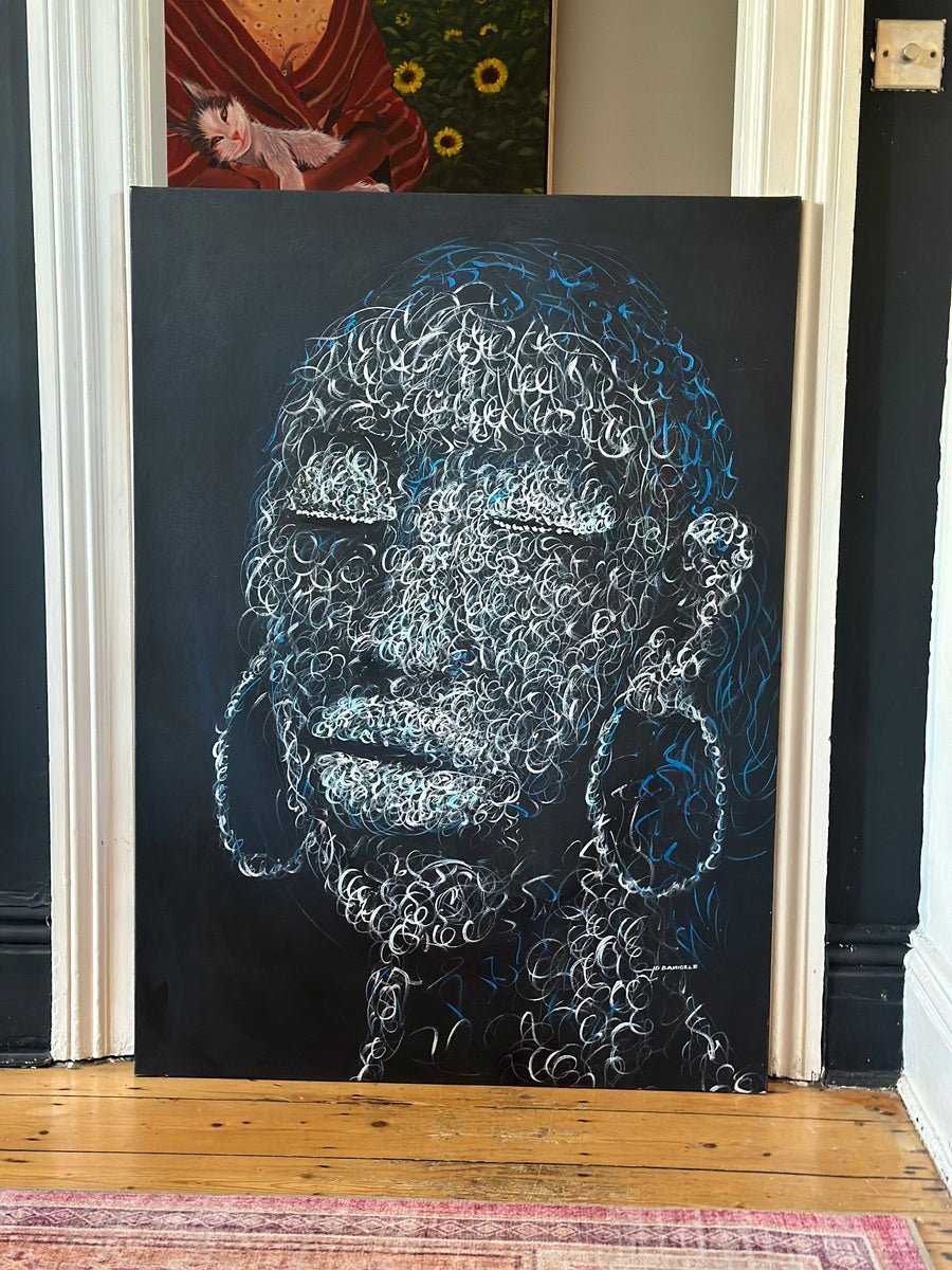“Circle of purity” by Bamidele is a modern hand-signed painting featuring a face with swirling white and blue outlines, full lips, and large hoop earrings on a black background. It leans against the wall on a wooden floor below another artwork.