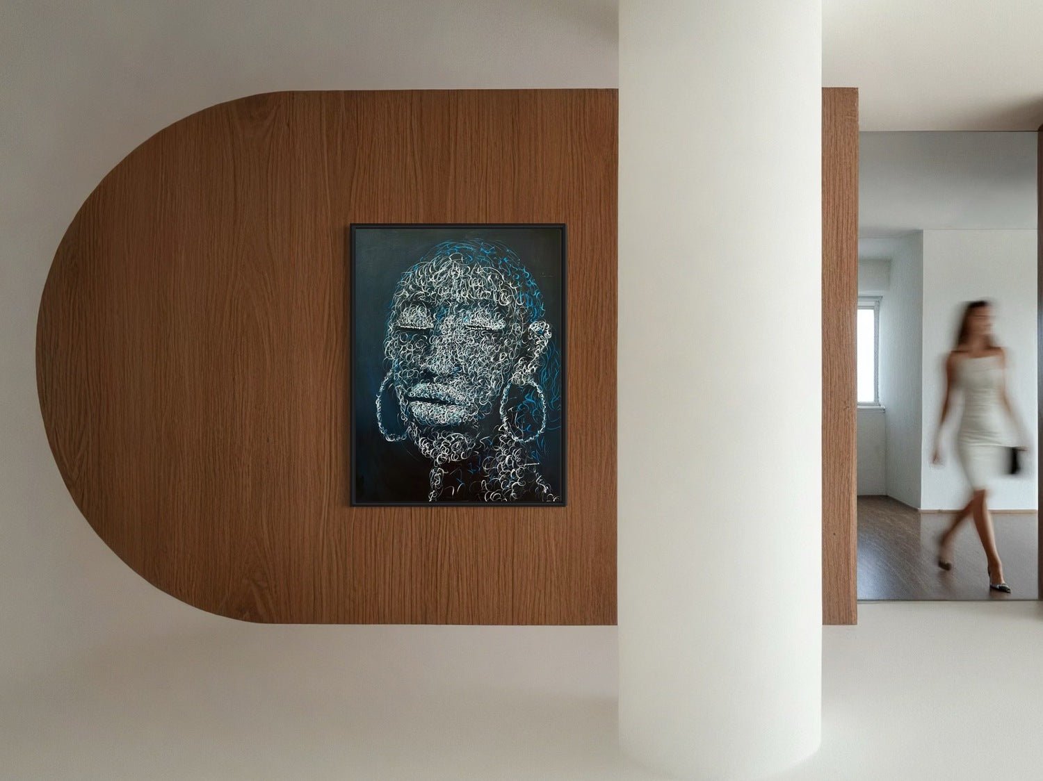 Circle of purity" by Bamidele, a framed acrylic on canvas abstract face portrait, hangs on a curved wooden wall as a blurred woman in white walks past on the right, with a white pillar partly obscuring the unique artwork.