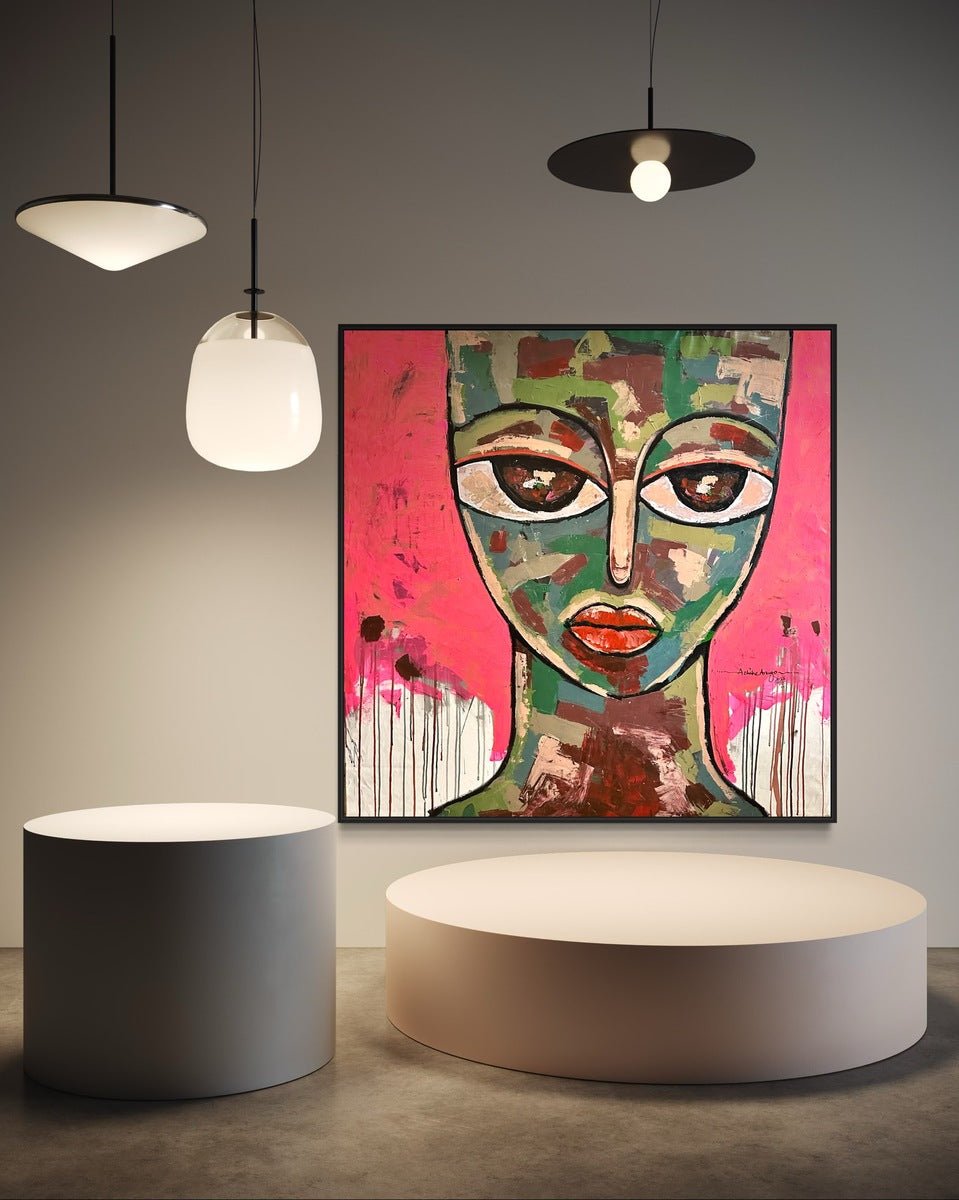 A modern gallery space showcases "Emancipation 1" by Achike Anayo: a large, colorful acrylic painting of a face with exaggerated features on vivid pink, displayed alongside two round white platforms and three hanging lamps.