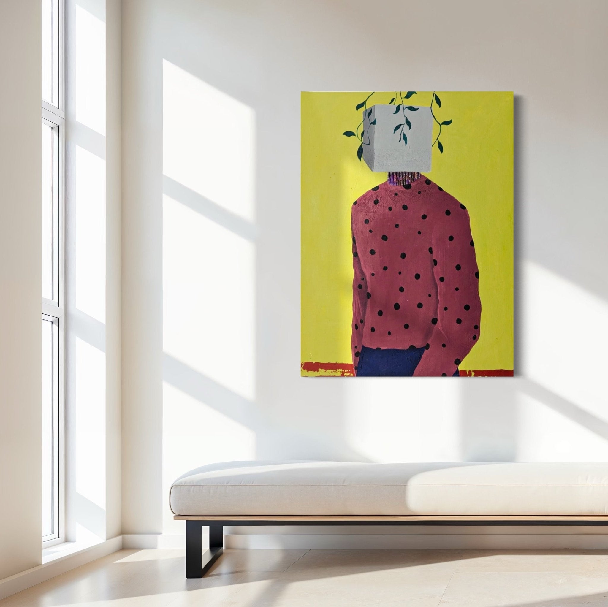 A modern, minimalist room with a white bench and large window features "Embody II" by Slam Austin—an acrylic on canvas showing a person in a red polka-dot shirt, head hidden by a white block with green vines, set on bright yellow.