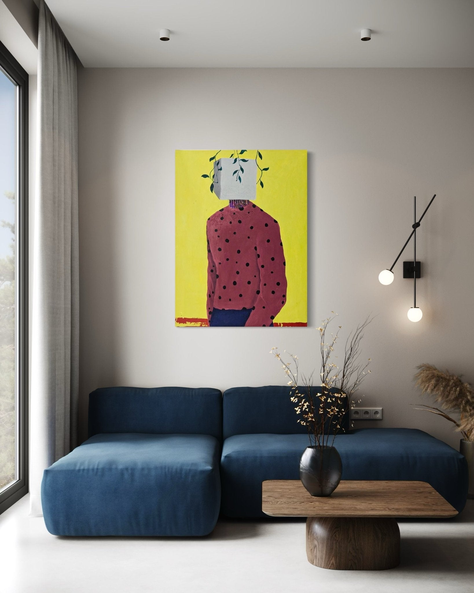 A modern living room with a blue sofa, wooden coffee table, and "Embody II" by Slam Austin—an acrylic on canvas painting of a headless figure with leaves and a white box on its neck, set against yellow. Minimalist decor and natural light complete the space.