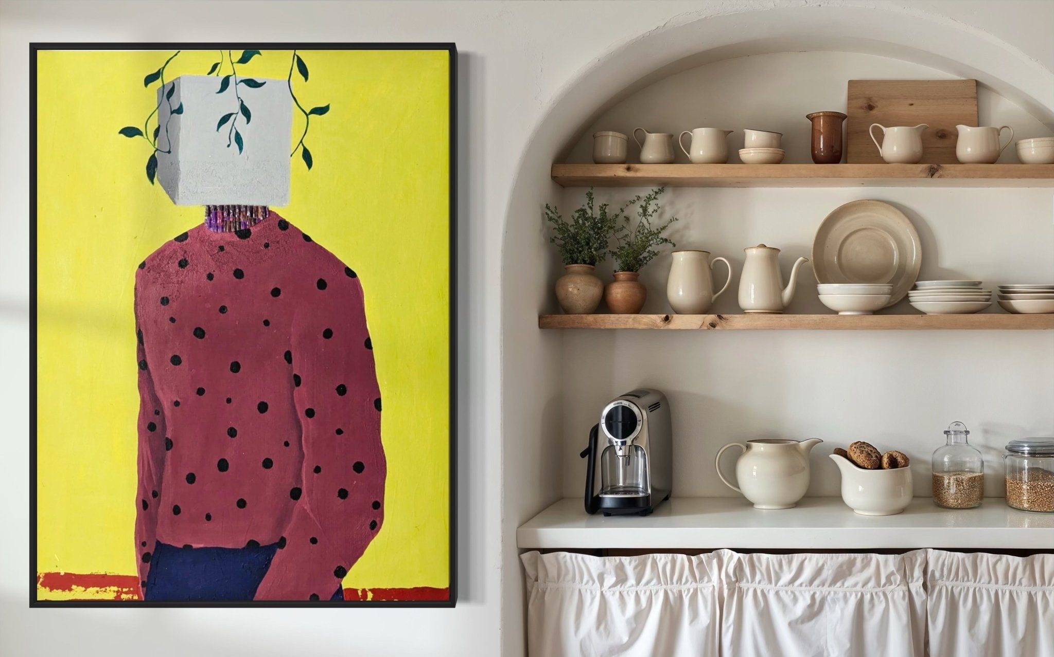 A kitchen with open wooden shelves displays dishes and ceramics. On the left wall is "Embody II" by Slam Austin, a vibrant acrylic painting of a figure in a polka dot shirt and plant-covered box head on a yellow background.
