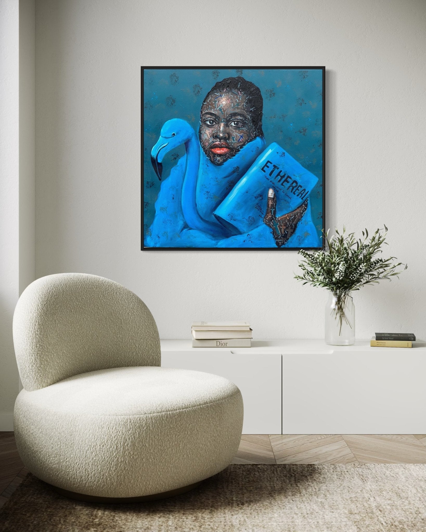 A modern living room with a white curved chair, low white cabinet, vase with greenery, and 'Ethereal' from the Finding Self series—an original 91 x 91cm painting by Agboola Emmanuel I—depicting a person with a blue book labeled ETHEREAL.