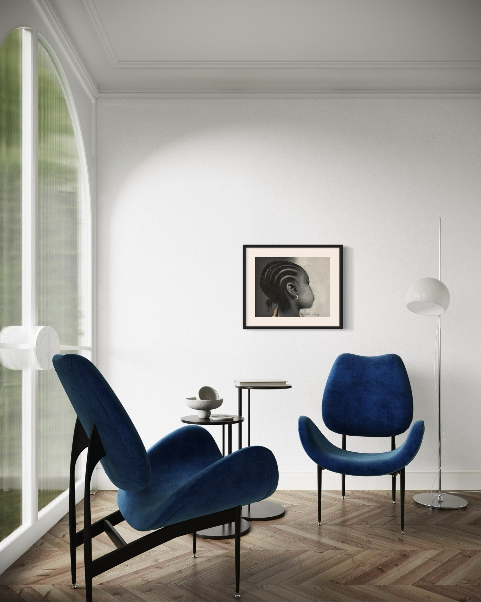 Modern minimalist living room with two blue velvet chairs, round side table, sculptural floor lamp, and Kehinde Badmuss’s "Ewa" Young Girl With Earring acrylic portrait on the white wall. Large arched window floods space with light.