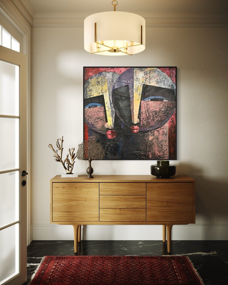 A modern entryway features a wooden console table with decor, a red patterned rug, and "Eye Contact," a large textured painting by Christopher Ankeli, illuminated by a white and gold chandelier.