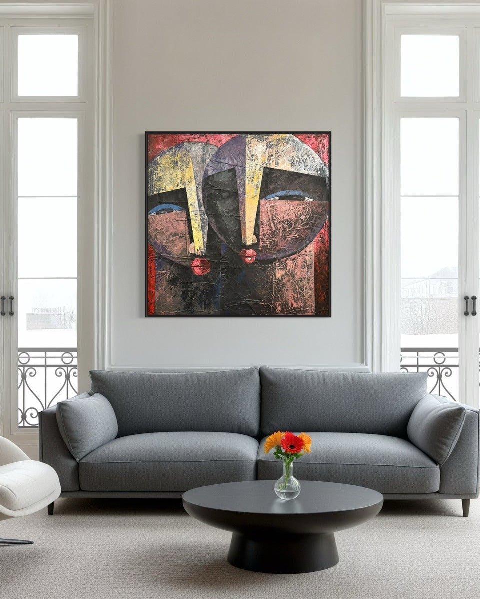 A modern living room with a gray sofa, round black coffee table and vase, plus "Eye Contact" textured painting by Christopher Ankeli—a bold abstract acrylic of two faces—on the wall between tall windows.