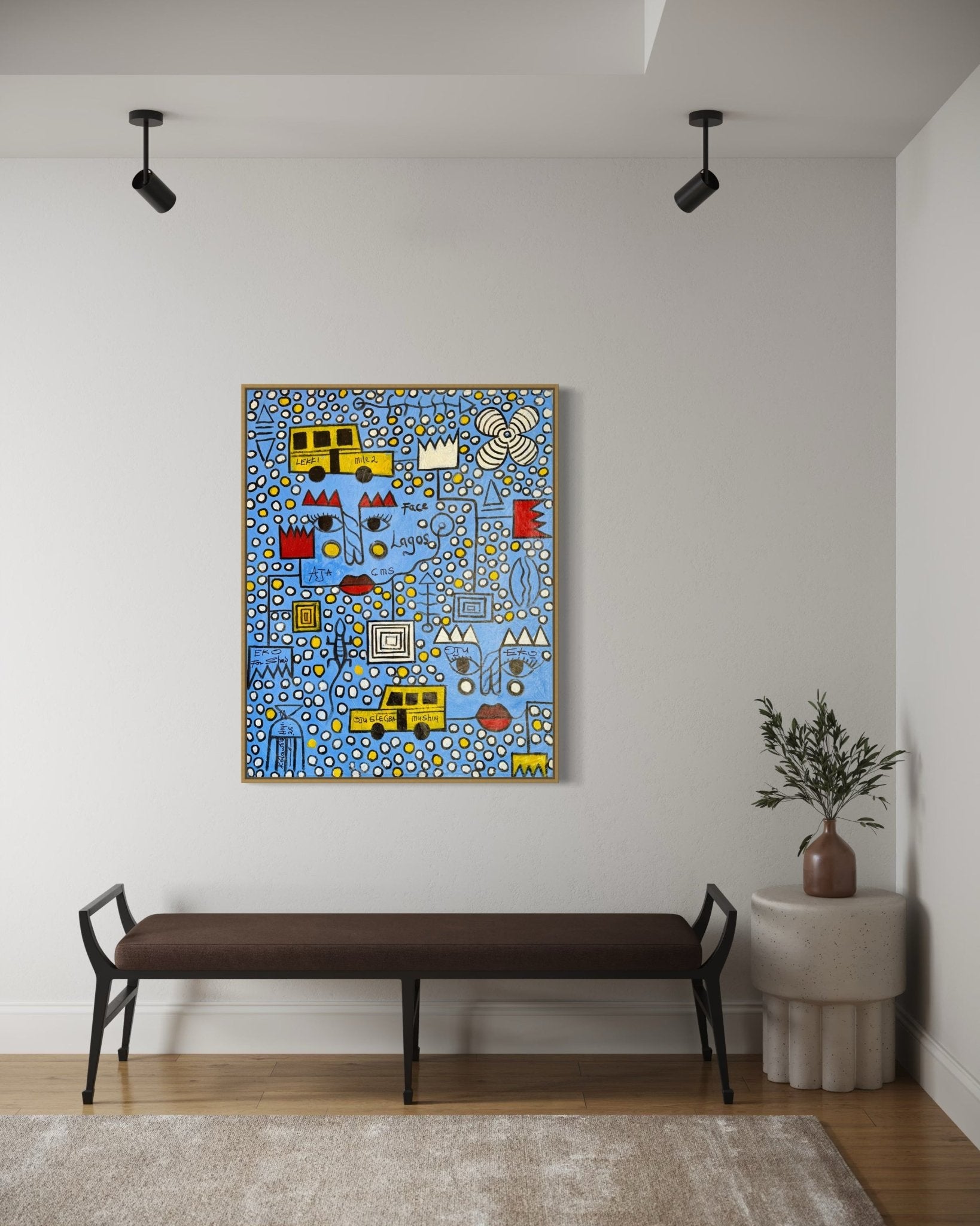 Face Of Lagos" by Kolawale Niyi, a colorful abstract painting with bold shapes, hangs above a dark bench on a white wall; track lighting and a small plant on a round table add modern minimalism to the space.