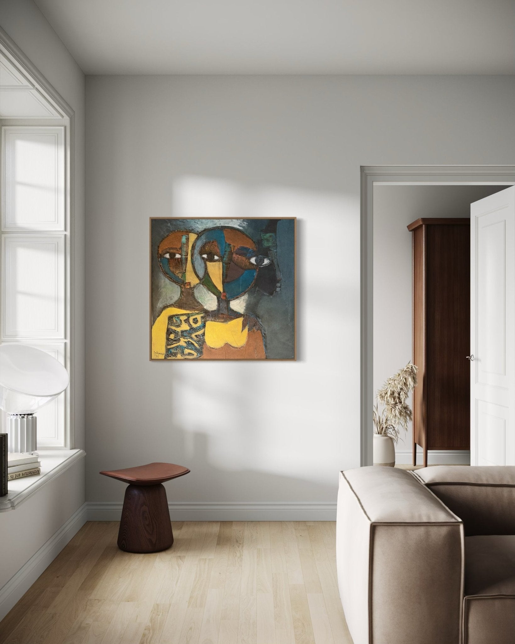 A modern living room with light walls, a large window, a beige sofa, and a small wooden stool topped by "Faces in the heart," an abstract hand-signed painting by J.O. Aransiola featuring faces in warm and dark tones with a certificate of authenticity.
