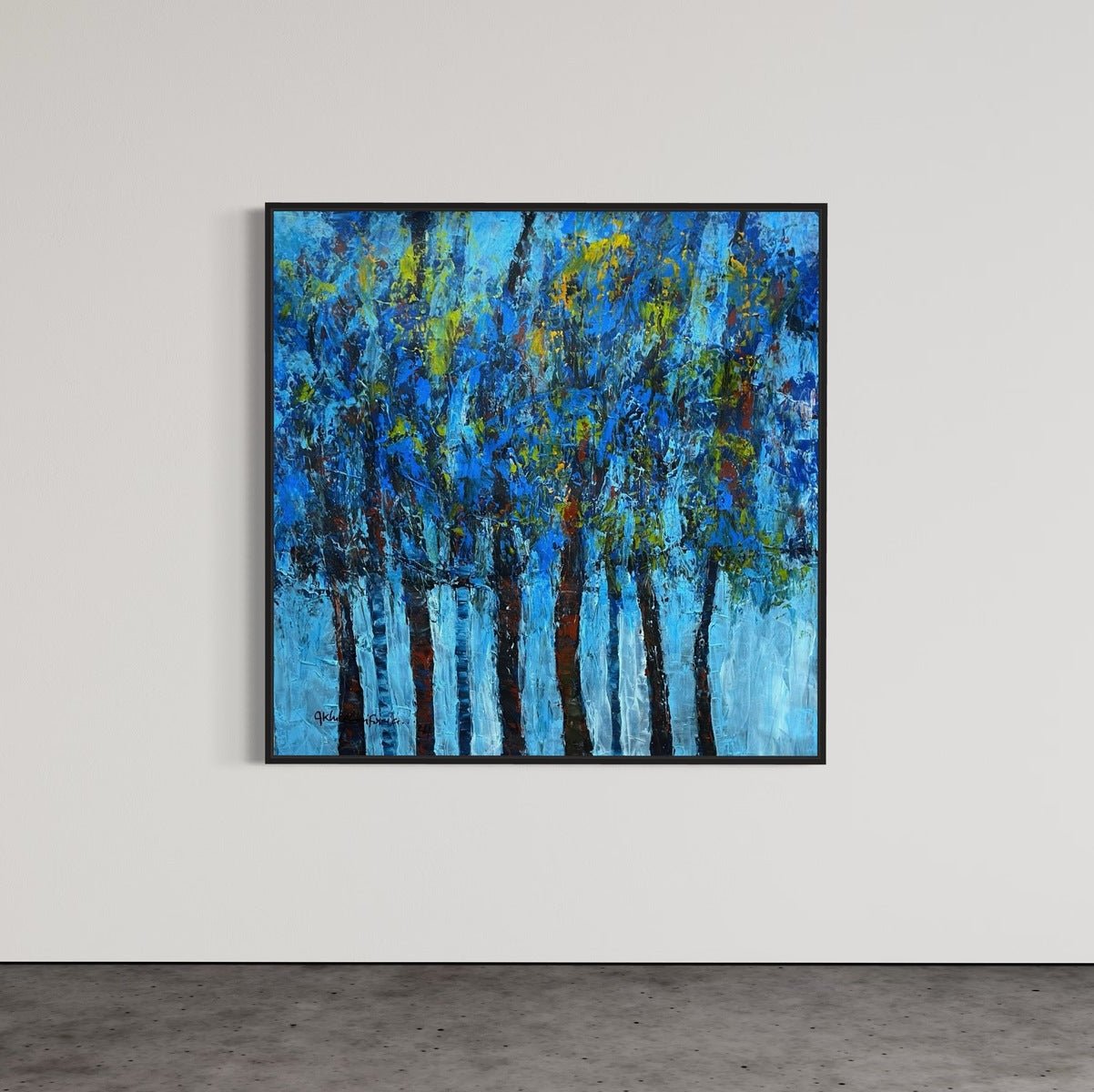 The Extra Large Textured Impasto Nature Painting "Growth" by Akhile Ehiforia features tall trees with blue and green foliage and brown trunks, framed and displayed on a white wall above a gray concrete floor.
