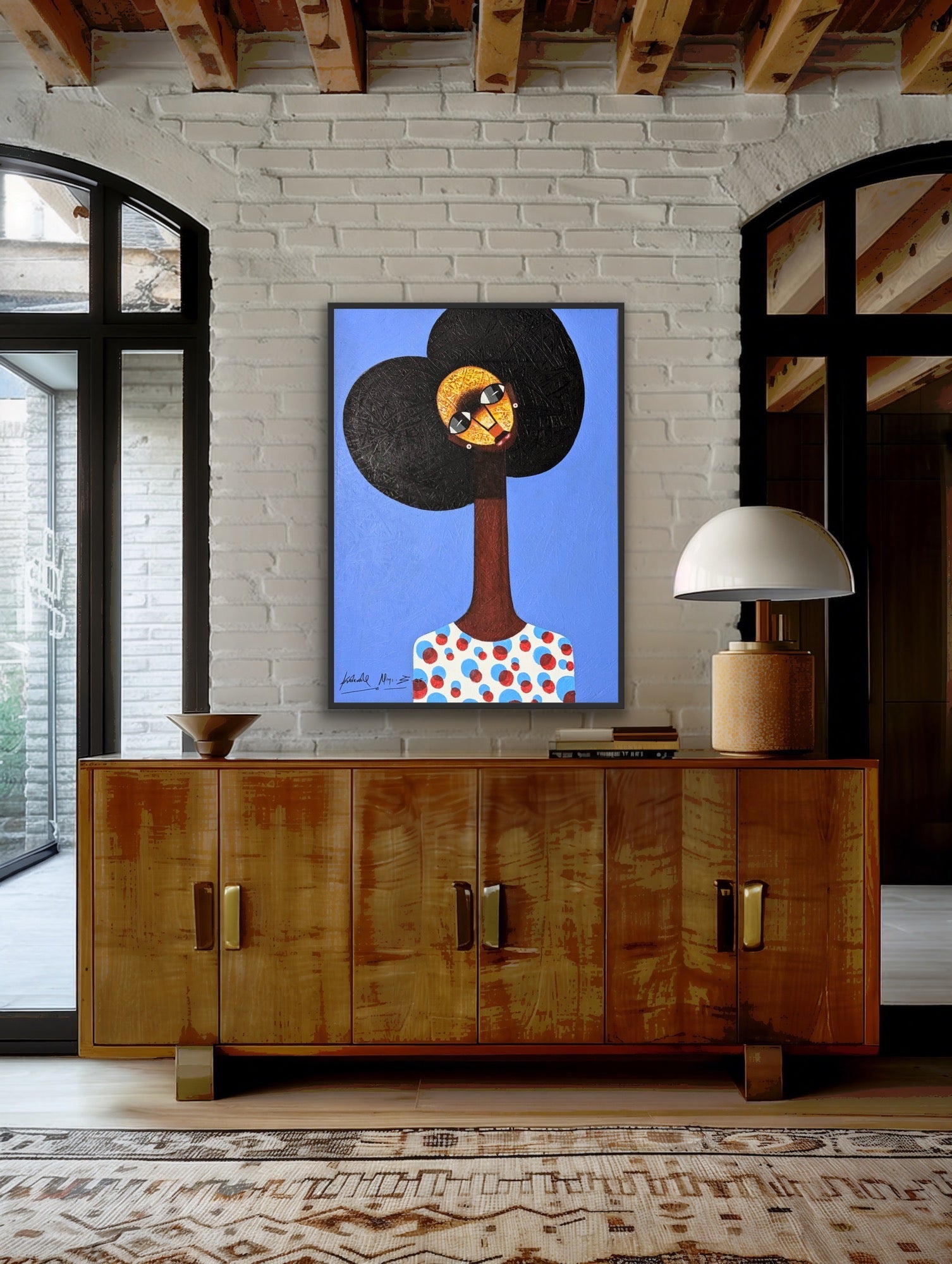 A modern living room features a wooden sideboard with decor, topped by Kolawale Niyi’s "Charming Cubist Portrait With Textured Details"—a vibrant acrylic on canvas of a woman with an afro—adding character to the white brick wall as sunlight streams through large windows.