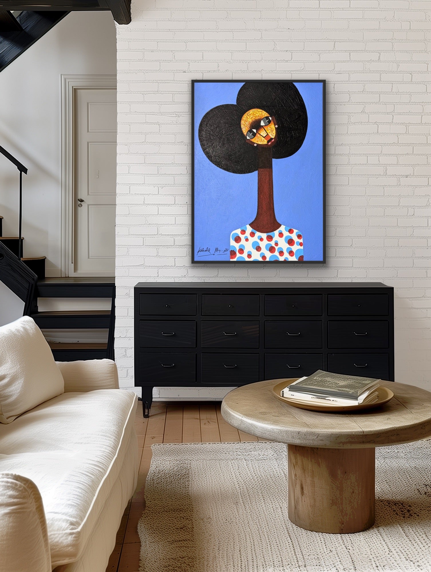 A modern living room features a white sofa, round wooden coffee table, and black dresser. Above the dresser hangs the Kolawale Niyi Charming Cubist Portrait With Textured Details by Kolawale Niyi on a white brick wall. Stairs and door in background.