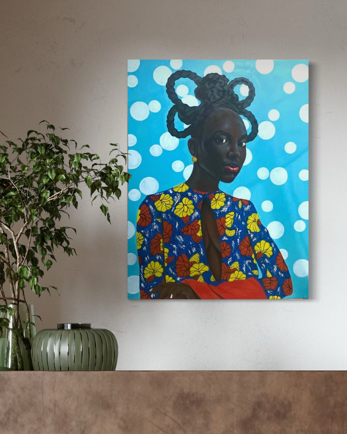 Enigmatic Beauty: 'Lady' by Ajenifuja Abiodun—a vibrant portrait of an African woman—hangs above a wooden shelf adorned with a green plant in a ribbed vase and a small glass container, celebrating contemporary African art.
