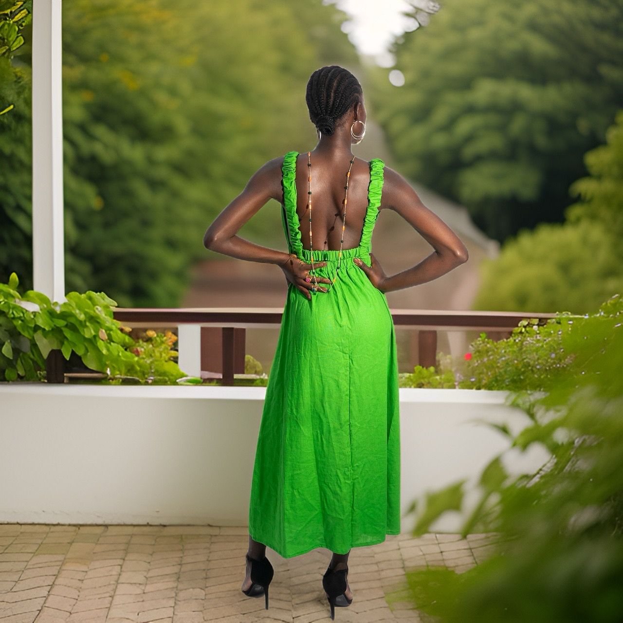 A woman in a bright green Linen Cutout Dress from bibianna.co.uk stands on a patio among lush greenery. With braided hair, hoop earrings, and black heels, she showcases a chic summer style surrounded by trees and a winding path.