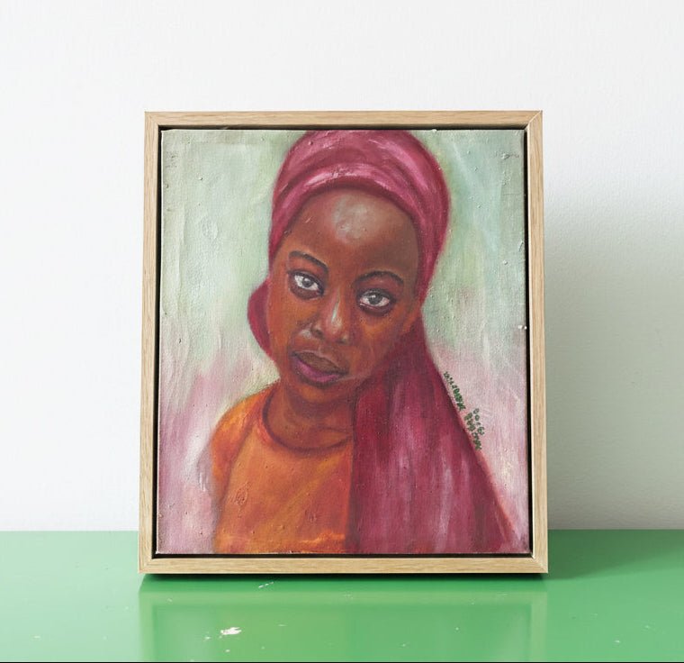 Little Amina" by Bibianna African Art Collective is a framed expressionist oil portrait of a woman in a red headscarf and orange top, displayed on a green surface with shelves and assorted objects in the background.