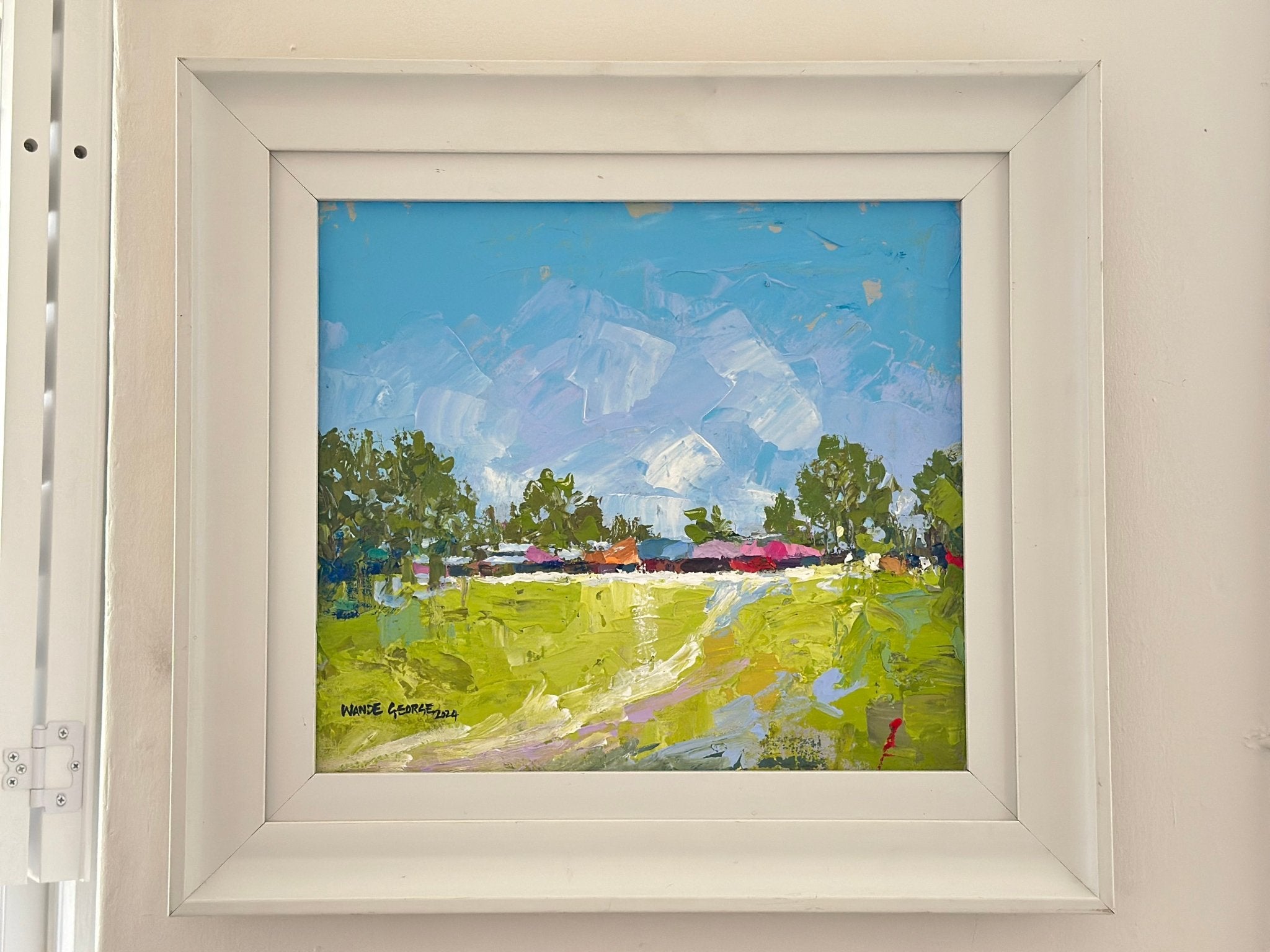 Long Awaited Visit" by Wande George is a hand-signed, framed acrylic painting featuring bold textures of green fields, scattered trees, and a blue sky. The contemporary artwork comes in a white frame and brightens any light-colored wall.