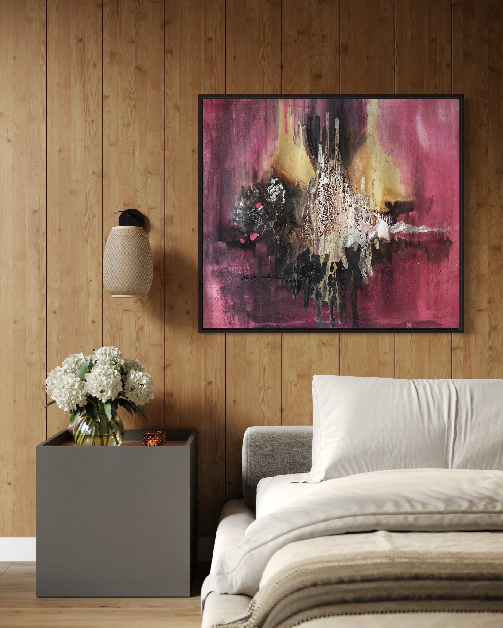 A cozy bedroom with a wood-paneled wall, modern gray bed, side table with white flowers, and 'Majority', a large hand-signed abstract painting by Soji O in pink, yellow, and dark tones—includes certificate of authenticity.