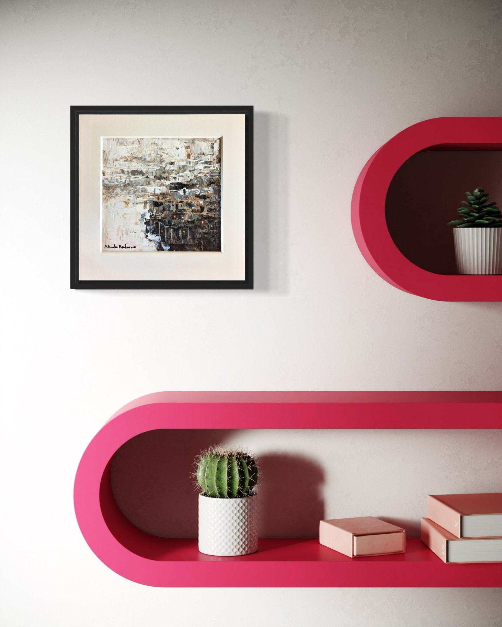 A minimalist wall features a hand-signed, framed Miniature Abstract Landscape by Kehinde Badmuss, with pink oval shelves displaying a potted cactus, succulent, books, and two pink boxes. The modern decor feels unique and organized.