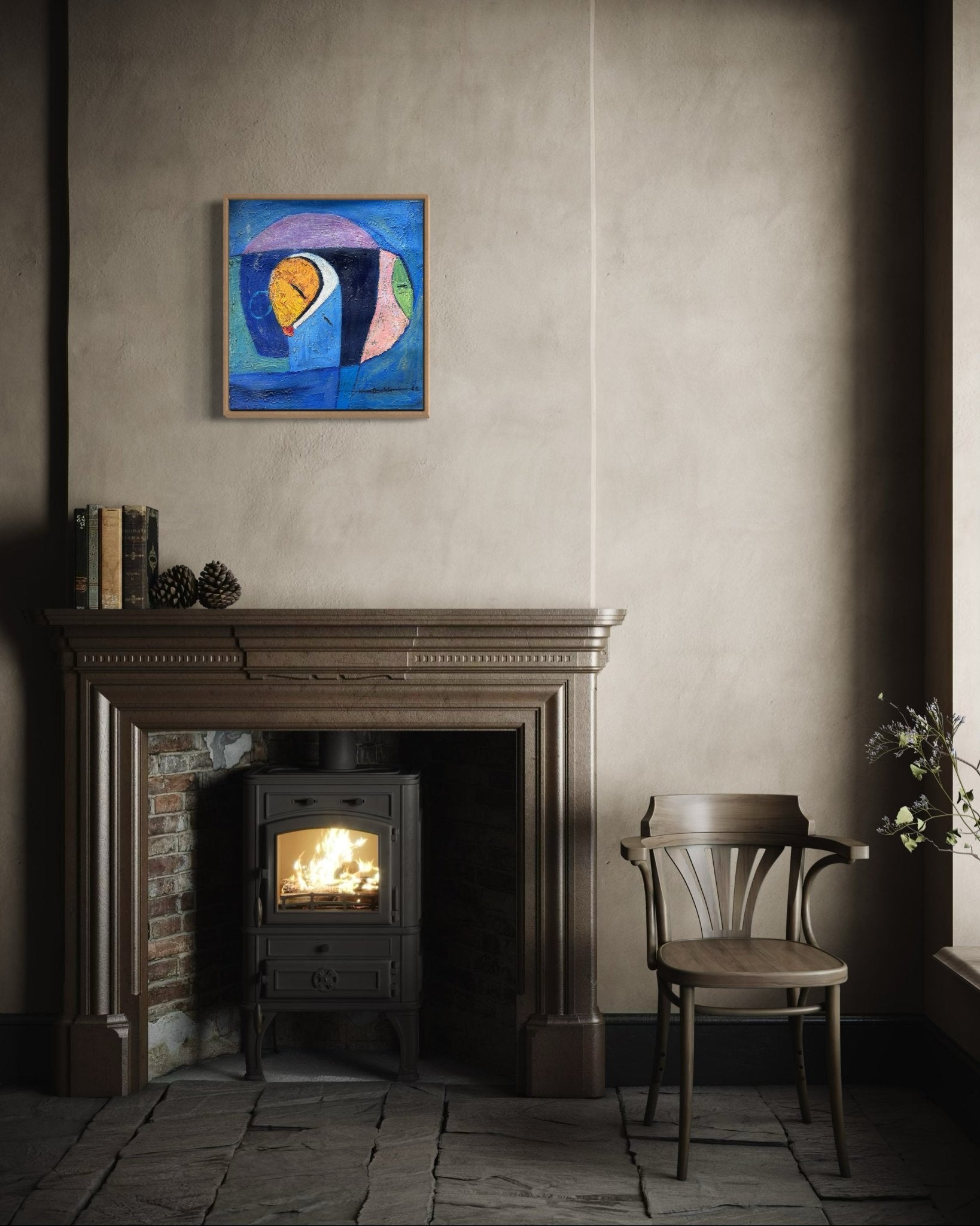 A cozy room features a wood stove in a rustic fireplace, a wooden chair, books and pinecones on the mantel, and the NOSA OSADOLOR Miniature Textured Abstract painting in a framed oak tray frame hanging above.