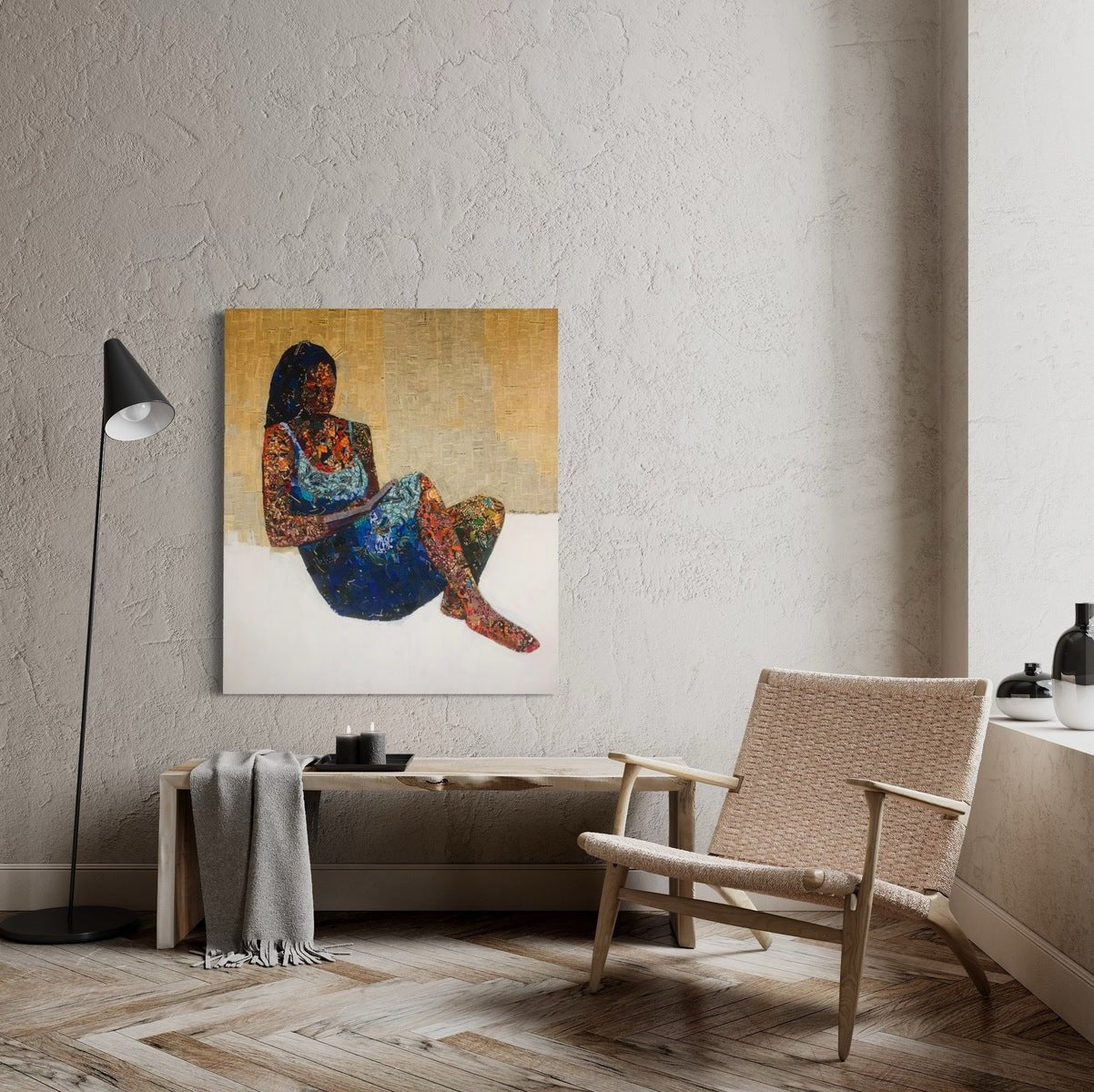 A modern living room features a woven chair, floor lamp, side table, gray blanket, and minimalist decor. Above the chair hangs Seye Morakinyo's "Love Book," a mixed media painting of a woman in pages of writing.