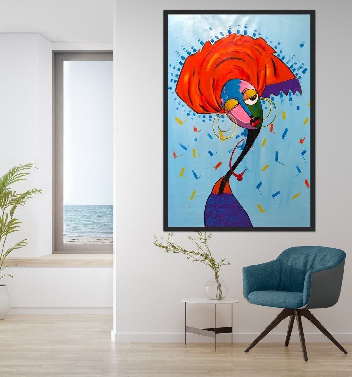 A modern room with a blue chair, side table, potted plant, and ocean view. “My Gele” by Afuope Opeyemi—a colorful abstract portrait of a woman in a red headscarf—hangs on the wall, hand-signed with a certificate of authenticity.