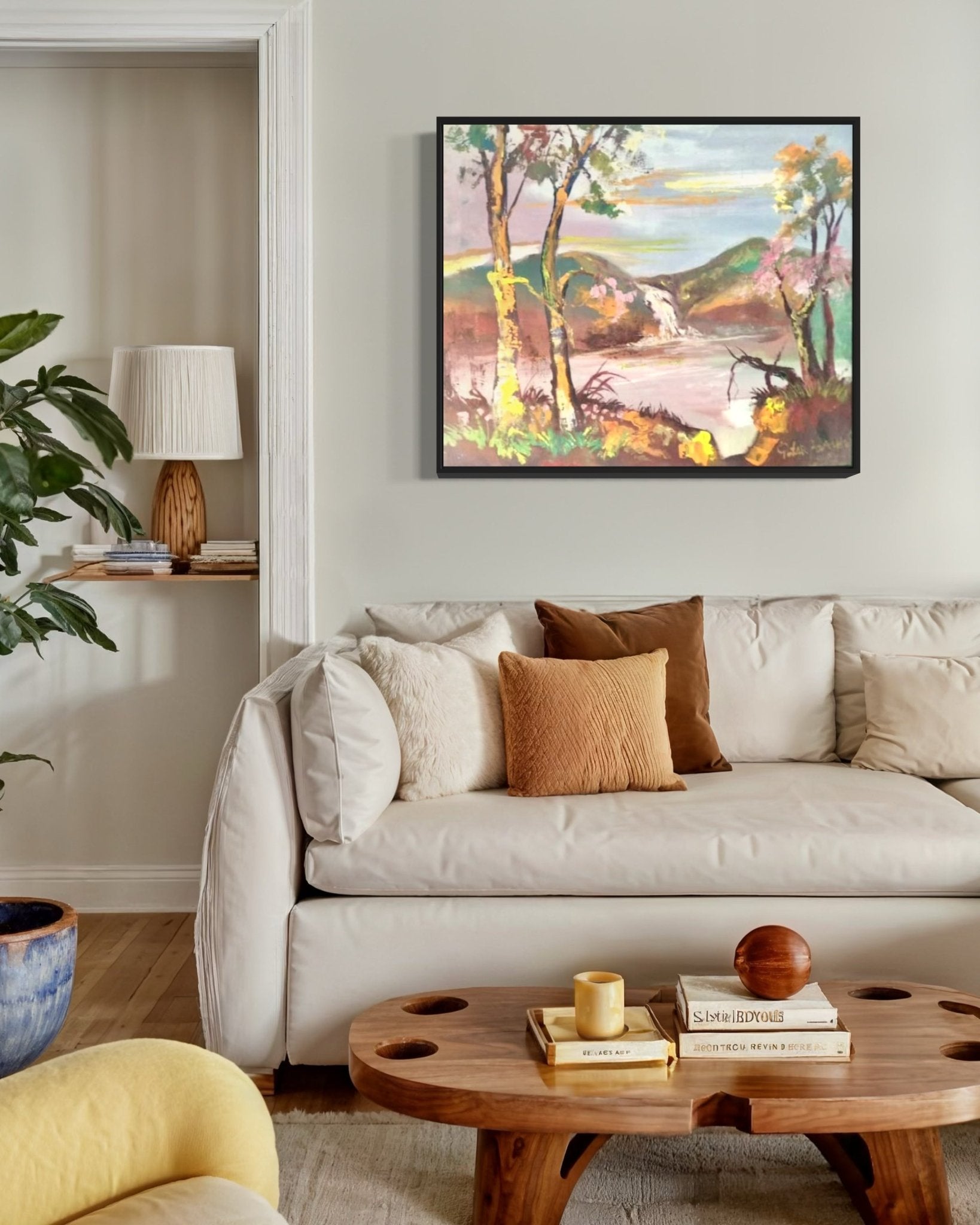 A cozy living room with a beige sofa, wood coffee table, earth-tone pillows, potted plant, and "Nature" Original Landscape Painting by Pitar Alakhume—complete with Certificate of Authenticity—on a light-colored wall.