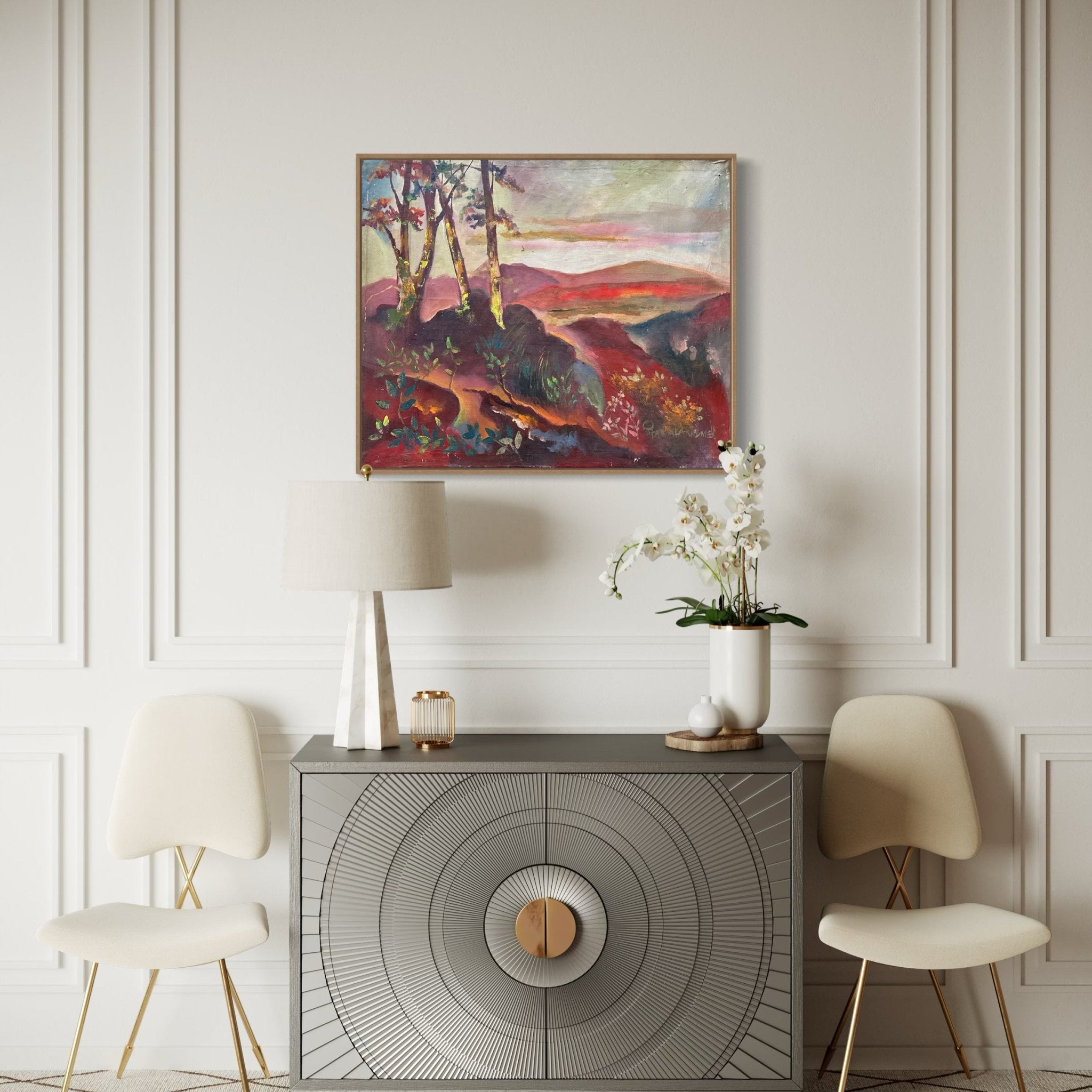 A modern room with two white chairs, a gray cabinet with a circular pattern, a white lamp, and an orchid. Above the cabinet hangs "Nature II," an original landscape oil painting by Pitar Alakhume featuring trees and hills.