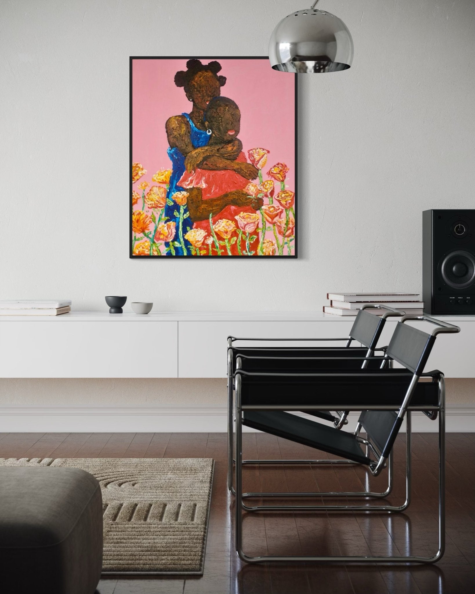 A modern living room features black chairs, a white cabinet, and "Companion. Acrylic on Canvas" by Ola Kuti—a painting of a woman with a child amid flowers on pink. A metallic hanging lamp and a speaker are also visible.