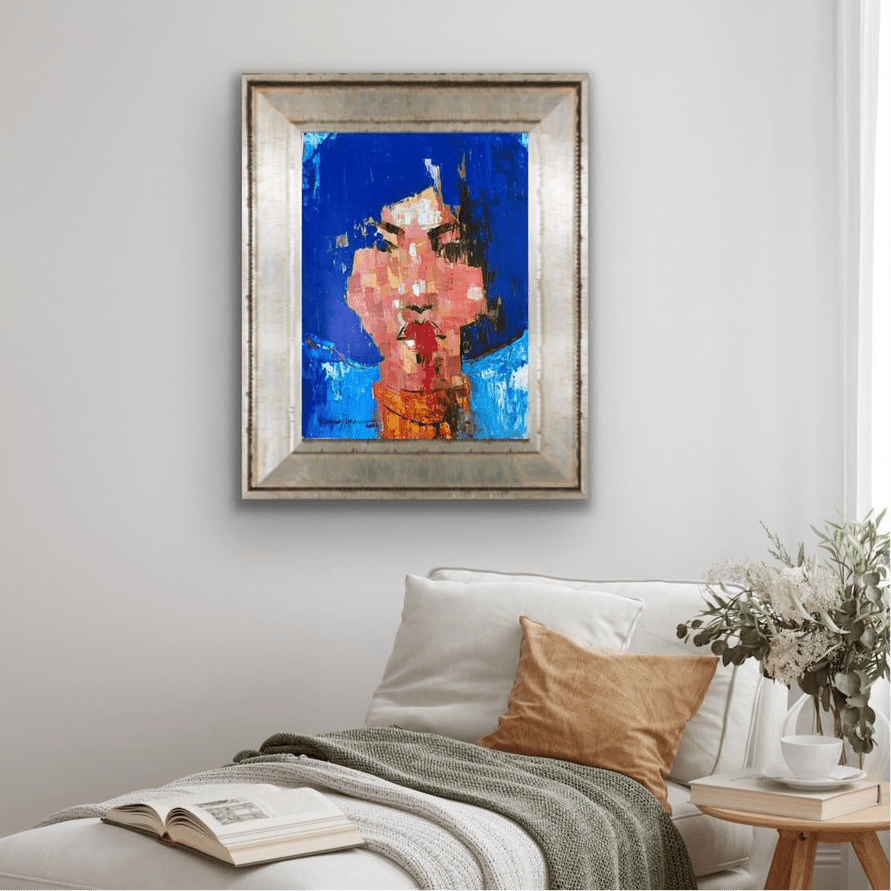 “One of a Kind Series by Olasunkanmi Oyelusi, an abstract acrylic face painting in bold blue, pink, and orange, decorates the space above a couch with white and tan pillows, a green throw blanket, and a side table with a potted plant.”.