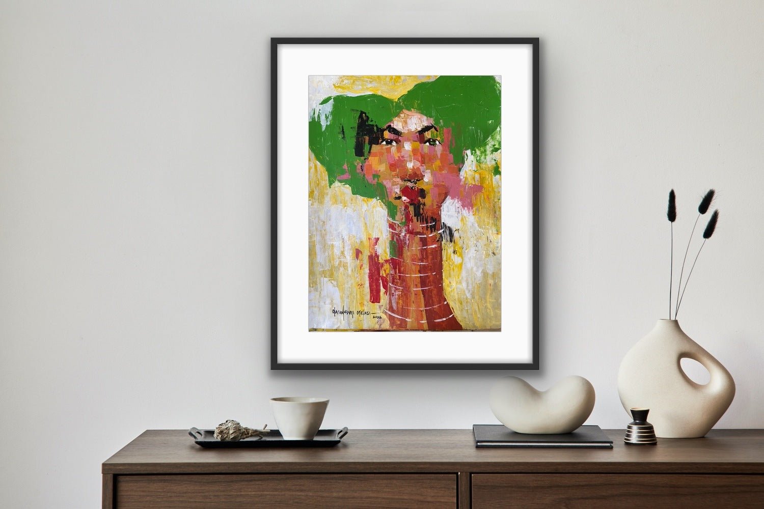 “One of a Kind Series by Oyelusi, an original acrylic on paper by Olasunkanmi Oyelusi, featuring bold green, yellow, and red brushstrokes, hangs above a modern console table with minimalist white ceramics and a cup.”.