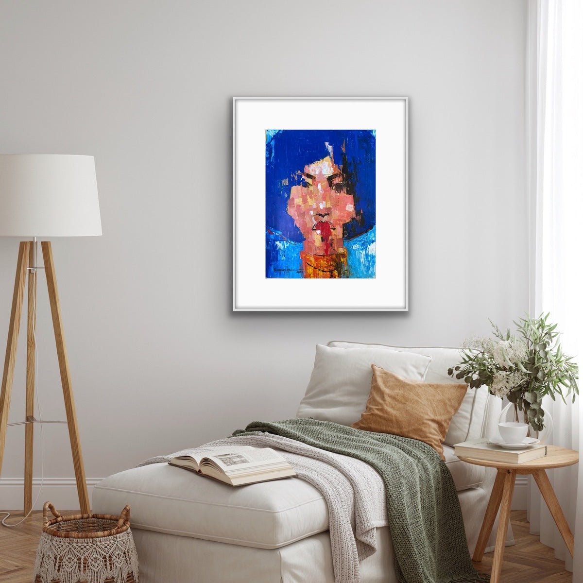 A modern living room features a white lounge chair, green throw, pillows, floor lamp, potted plant, and an original “One of a Kind Series by Oyelusi” abstract portrait (blue and pink acrylic on paper) by Olasunkanmi Oyelusi framed above the chair.