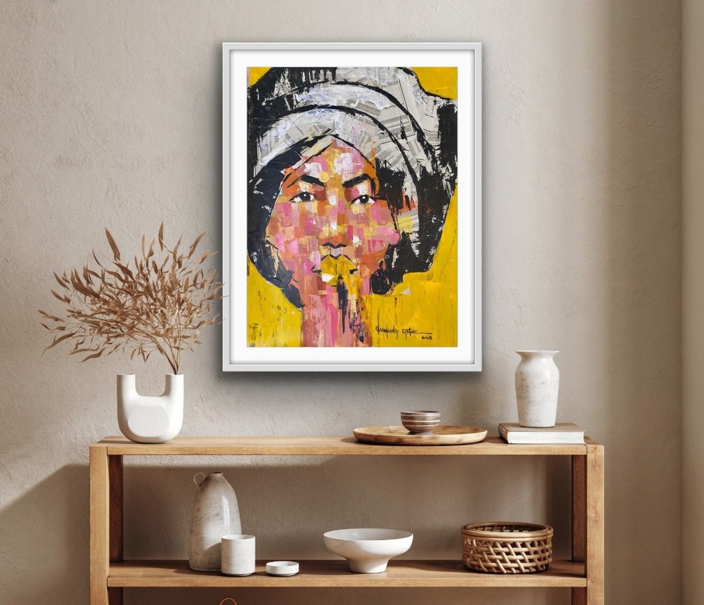 From the One of a Kind Series by Olasunkanmi Oyelusi, this hand-signed abstract portrait showcases a vibrant face with a head covering, displayed above a wooden console with minimalist ceramics and dried plants.