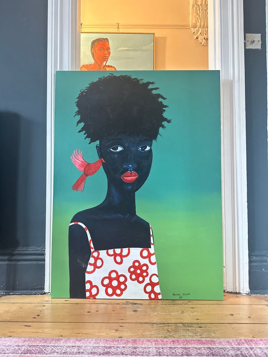 Phoenix" by Afuope Opeyemi is an expressive, hand-signed acrylic portrait of a Black child in a white dress. The artwork is propped against a wall, with another portrait by Afuope Opeyemi visible in the background.