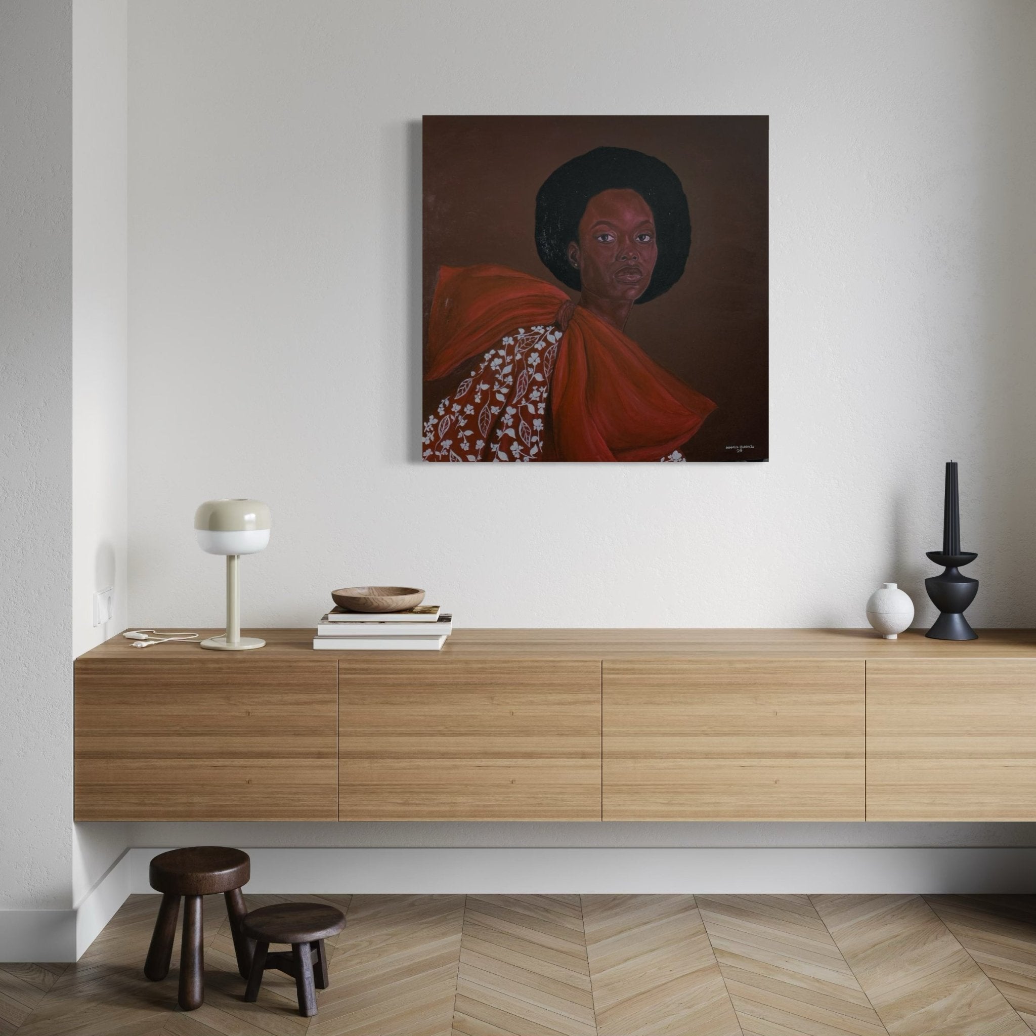 A modern wooden sideboard with books, decor, and a lamp sits beneath Portrait by Hammed Omobayo (Hammed Olayanju Omobayo) on a light wall. Two small stools are placed in front of this striking artwork featuring a woman in a red dress with an afro.