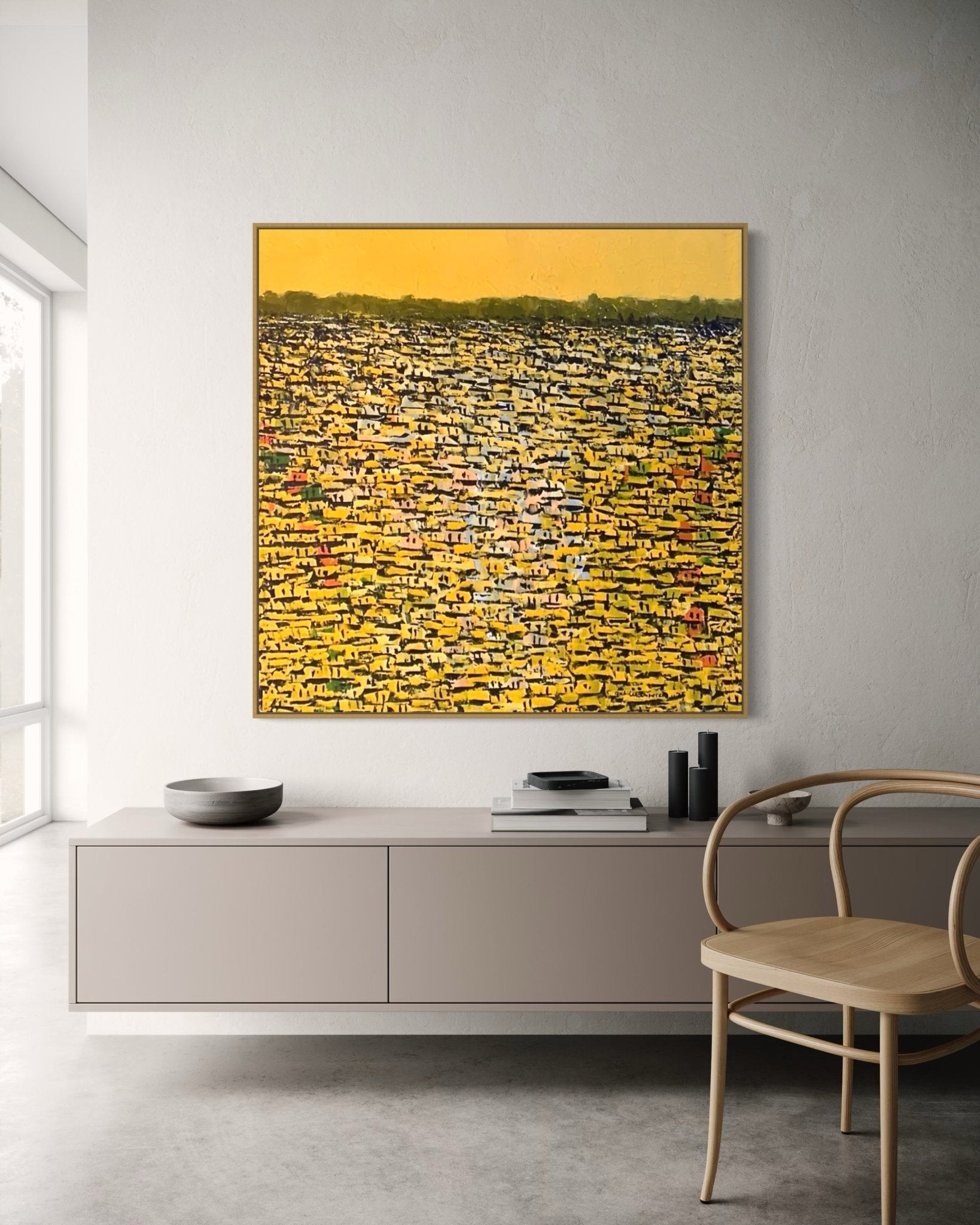 A minimal modern room featuring a light sideboard, wooden chair, and "Rooftops Series," an abstract acrylic on canvas by Akhile Ehiforia in yellow, black, and white tones, hanging on a light wall with soft natural light from a tall window.