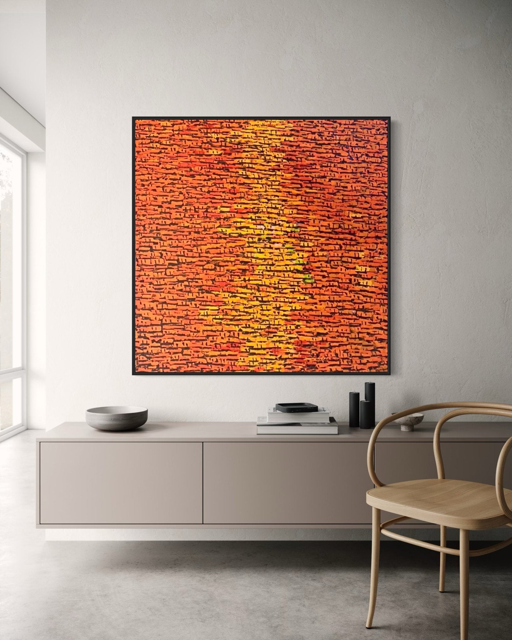 A modern living room with a light gray sideboard, wooden chair, and a large Akhile Ehiforia "Rooftops" Series abstract acrylic painting in orange and red with black lines, hand-signed by the artist, hanging on a white wall lit by tall windows.
