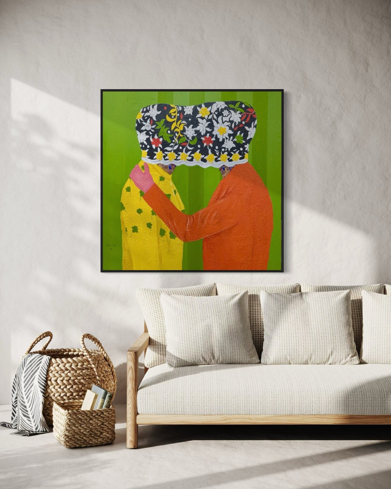 A modern living room with a beige sofa, pillows, woven baskets, and "Secrets" (122 x 122cm) by Slam Austin—an acrylic painting of two figures with floral-patterned heads—hanging on a green wall above the sofa.